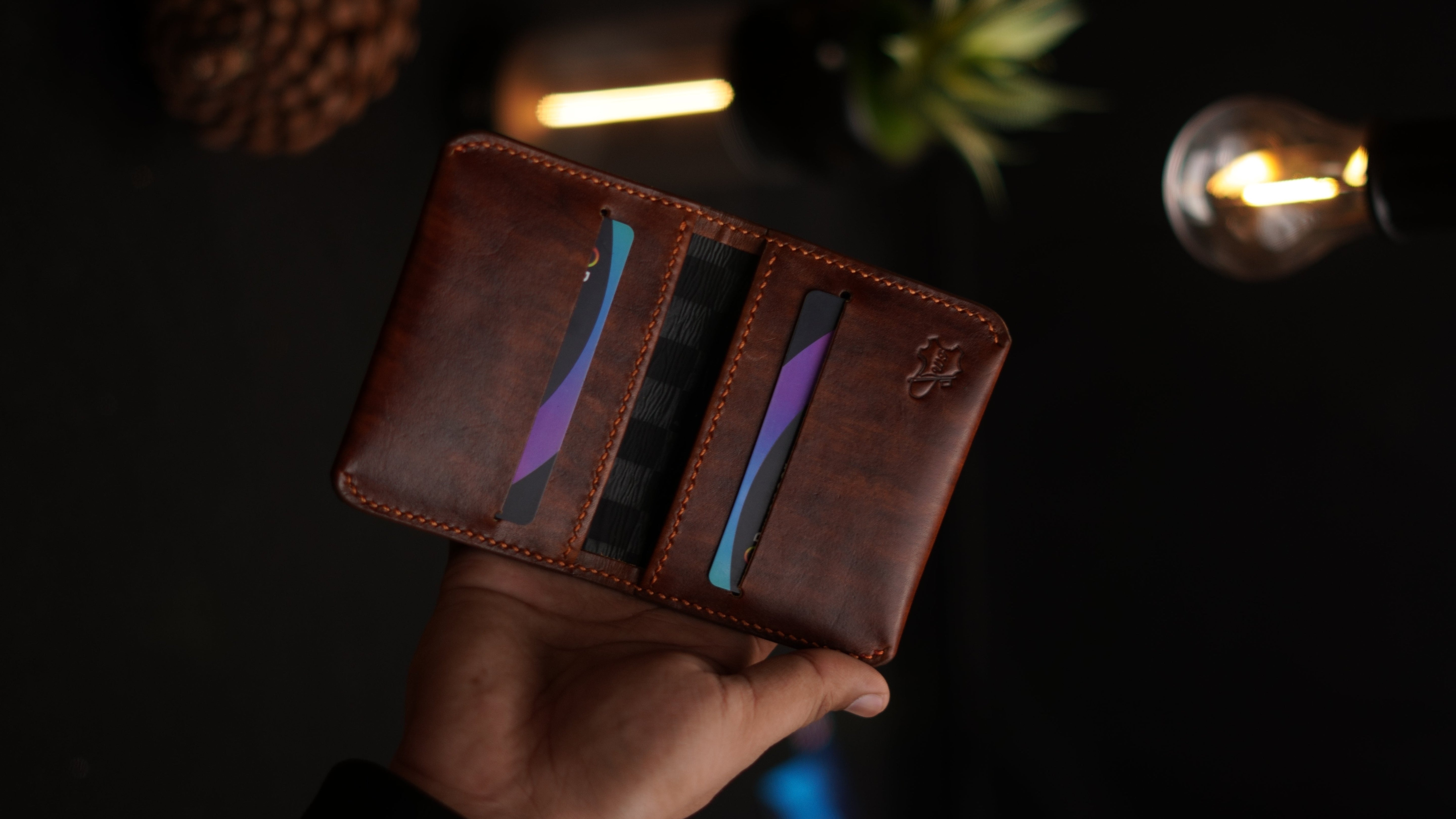 Brown leather wallet with card slots held by a hand against a dark background